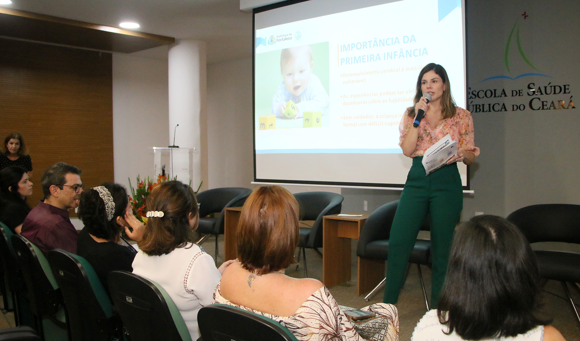 primeira-dama falando ao microfone em cima de palco para pessoas sentadas à frente